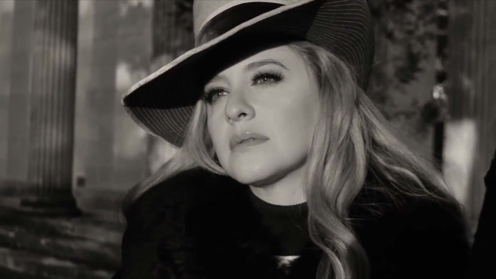 Black and white film frame, Jenilyn in a fedora among columns