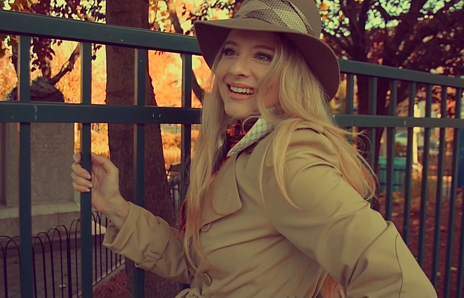 Autumn portrait in a trench coat and hat by a park fence